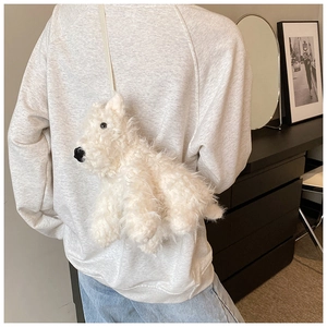 Dettaglio della borsa a tracolla in peluche bianco a forma di cane indossata da una persona