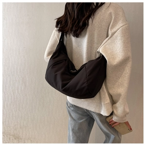 Gros plan d'un sac cabas demi-lune en nylon noir avec détails plissés sur la bandoulière