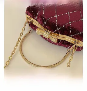 Détail du sac de soirée en velours bordeaux avec poignée dorée et fermoir nœud élégant