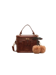 Détail de la texture cuir marron vintage et du pendentif cerise sur le sac à main