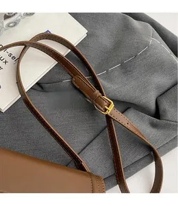 Detail of adjustable brown leather shoulder strap with gold buckle on crossbody bag