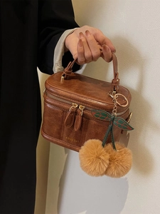 Détail d'un sac à main vintage en cuir marron avec breloque cerise et double fermeture éclair