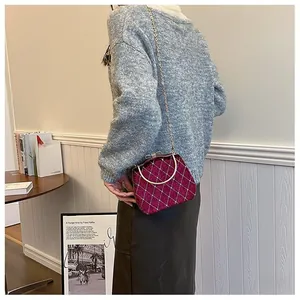 Détail du sac boîte matelassé bordeaux avec poignée dorée et bandoulière chaîne sur table