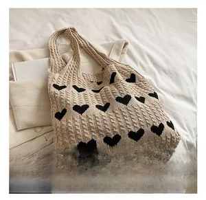 Macro detail of beige knit tote bag showing heart pattern and chunky cable knit texture