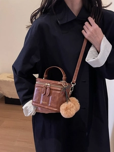 Détail d'un sac bandoulière en cuir PU marron avec logo doré et pompon en fourrure douce