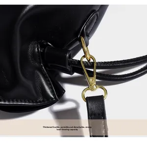 Détail du fermoir en métal doré poli sur la bandoulière d'un sac seau en cuir noir