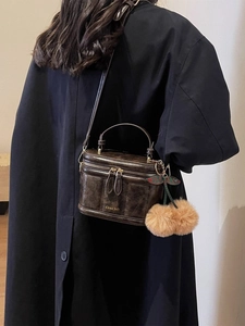 Détail d'un sac à main carré marron foncé en cuir ciré avec breloque cerise en fourrure