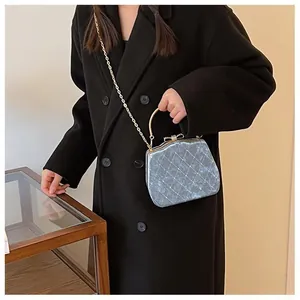 Détail du sac boîte bleu matelassé avec poignée dorée et fermoir nœud sur manteau noir