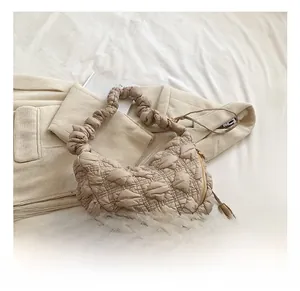 Detail of beige quilted crescent bag with ruffled handle and elegant gold zipper