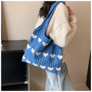 Detail of blue knitted tote bag with white heart jacquard and chunky cable knit texture
