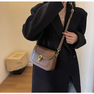 Detail of a brown faux leather saddle bag featuring a golden circular twist-lock buckle