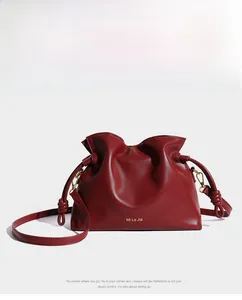 Détail du sac seau bordeaux plissé avec logo doré et bandoulière à nœud décoratif