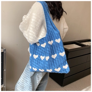 Detail of blue knitted tote bag with white heart patterns shown on a model's shoulder