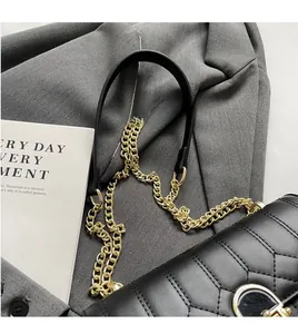 Detail der schwarzen Stepptasche mit goldener Kette auf grauem Anzugstoff