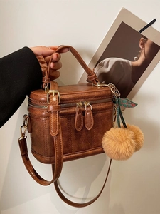 Détail d'un sac à main rétro marron avec pendentif cerise et fermetures éclair dorées