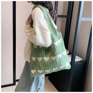 Macro detail of green knitted tote bag featuring white heart jacquard and cable knit texture