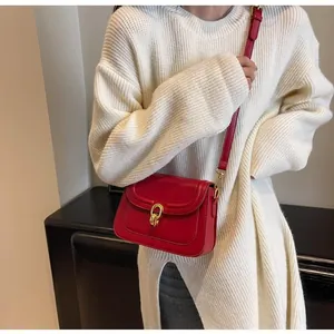 Detail of red leather crossbody bag with golden metal buckle and white knit sweater