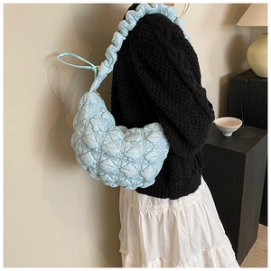 Detail of light blue quilted shoulder bag featuring ruffled straps and puffed texture