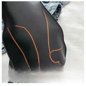 Detail of black leather bag with orange embroidery and striped woven shoulder strap