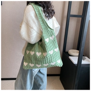 Detail of green knit tote bag featuring white heart patterns and cable knit texture
