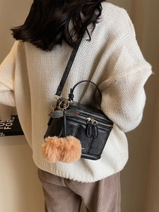 Détail d'un sac vanity en cuir noir avec un charmant pompon cerise sur un mannequin