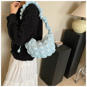 Quilted light blue puffy hobo bag with ruffled shoulder strap shown on model's shoulder