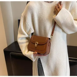 Brown retro shoulder bag with metal twist lock worn over a white knitted sweater