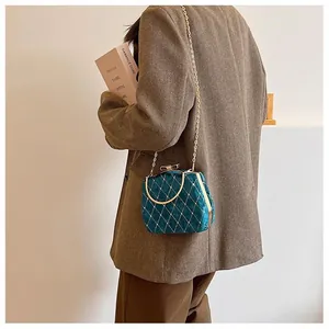 Sac boîte en velours vert foncé avec matelassage doré et bandoulière chaîne porté sur un blazer