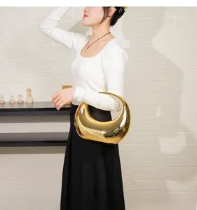 Detail of a gold mirror-finish sculptural handbag held by a model against a white wall