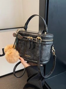Détail d'un sac cylindrique noir motif croco avec dorures et charms cerises peluche