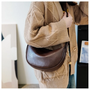 Detail einer dunkelbraunen Halbmond-Schultertasche aus Kunstleder auf einem Strickkardigan