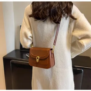 Brown leather crossbody bag with gold twist lock worn over a cream knit sweater