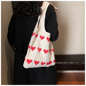 Detailed knit texture of large cream tote bag with red heart pattern shown on model
