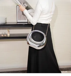 Close-up of a silver mirror acrylic handbag with a gold chain strap on a model