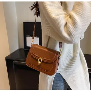 Caramel leather crossbody bag with golden twist lock shown on a white knit sweater