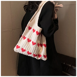 Detail of cream knit tote bag with red hearts and chunky cable stitch texture on model