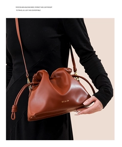 Sac seau en cuir marron mat avec logo doré porté par un mannequin dans un cadre chaud