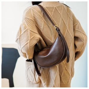 Detail einer braunen matten Leder-Halbmondtasche getragen mit beigem Strick-Cardigan