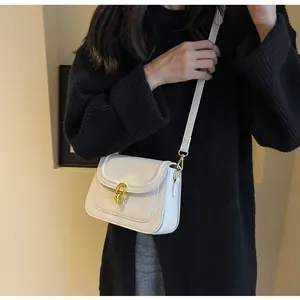 Detail of cream leather crossbody bag featuring a golden chain lock and adjustable strap