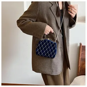 Détail d'un sac boîte en velours bleu marine avec chaîne dorée sur blazer en laine