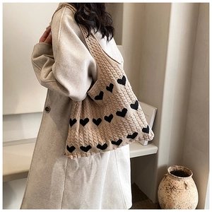 Detail of beige knit tote bag with black heart patterns and cable knit texture