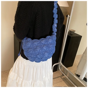 Detail of blue quilted puffer bag featuring pleated ruffled straps and textured fabric