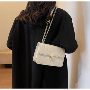 Detail der beigen Stepptasche mit V-Nähten und goldenem Metallverschluss am Gurt