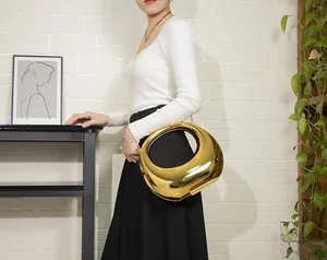 Chic gold metallic clutch bag with irregular oval design and cut-out handle on display