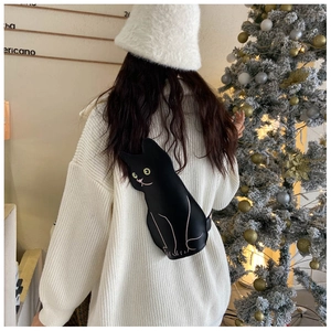Winter style black cat crossbody bag worn by model near a decorated Christmas tree