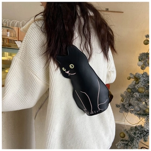 Detail view of a black cat-shaped crossbody bag with yellow eyes on a white knit sweater