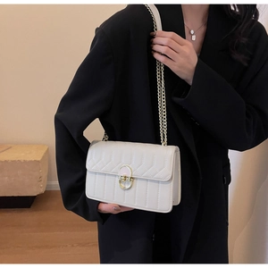 Detail einer weißen Stepptasche mit goldener Kette und Rundverschluss auf schwarzem Blazer