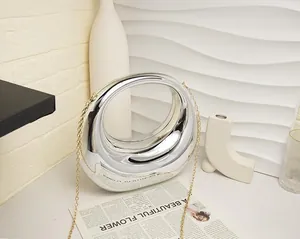 Detail of silver mirror acrylic handbag with unique curved handle and gold chain strap