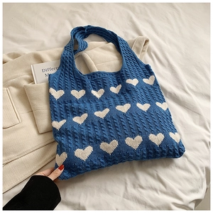 Close-up of cable knit texture and white heart pattern on a blue knitted tote bag