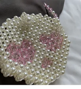 Close-up of handmade white pearl woven mini bag with pink floral accents and chain